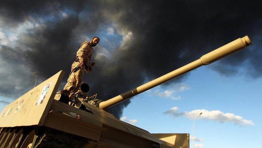 Un membre de l'armée libyenne sur un tank  à Benghazi le 23 décembre 2014, alors que des factions s'affrontent provoquant un incendie dans un stock de pneus