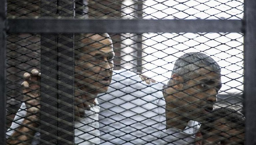 Les journalistes australien Peter Greste (g), canado-égyptien Fadel Fahmi (c) et égyptien Baher Mohamed écoutent la sentence prononcée contre eux depuis le box des accusés au tribunal de police du Caire, le 23 juin 2014