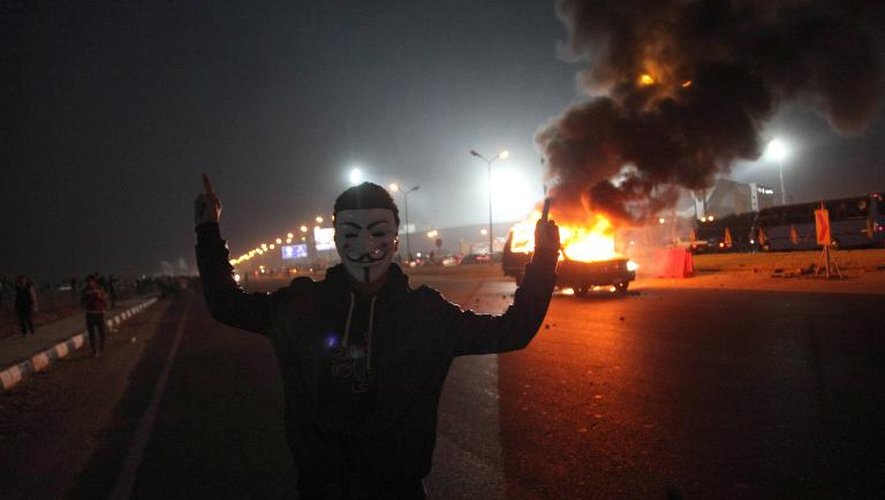 Un Egyptien portant un masque des Anonymous devant une voiture en feu près d'un stade du Caire le 8 février 2015