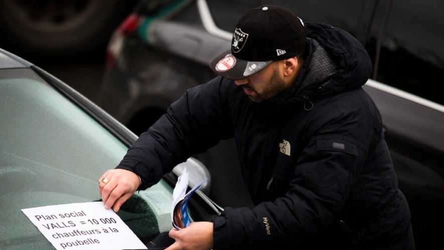 Un conducteur place une affichette "plan Valls - 10.000 chauffeurs à la poubelle" sur une voiture, lors d'une manifestation place de la Nation à Paris, le 9 février 2016