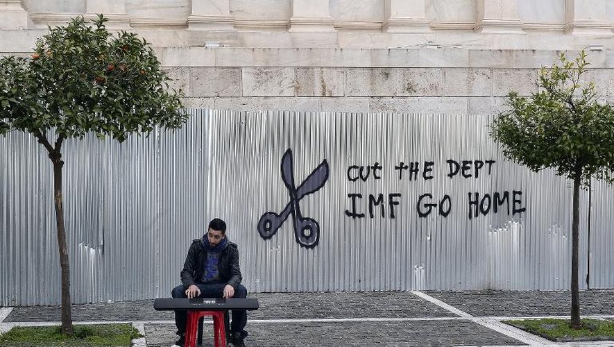 Un jeune musicien de rue joue devant un graffiti exigeant la réduction de la dette grecque et le départ du FMI, le 24 février 2015 à Athènes