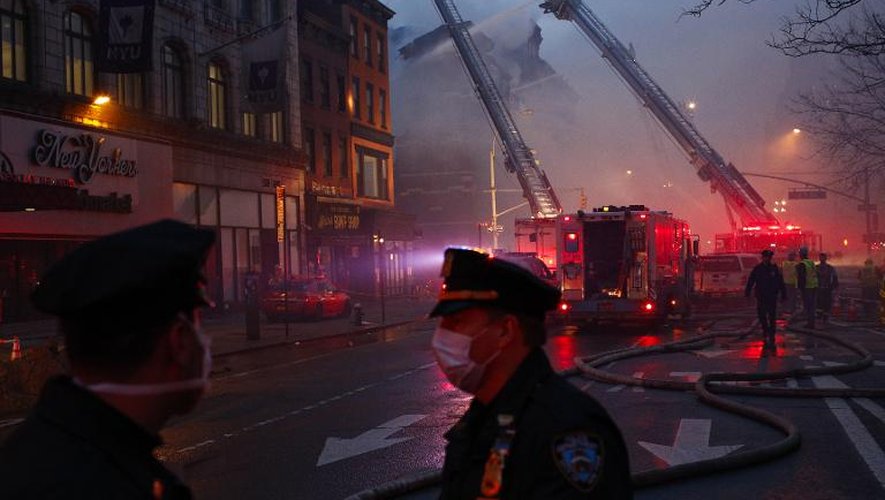 Des policiers new-yorkais devant les lieux d'un incendie avec en arrière plan les pompiers qui luttent pour circonscrire un incendie à New York le 26 mars 2015