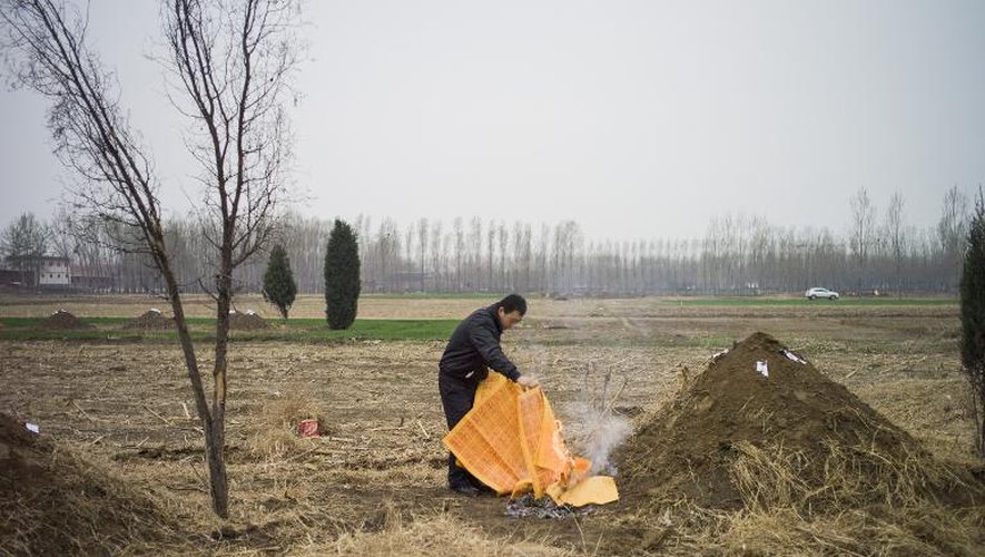 Un homme brûle des répliques de billets de banque devant un tumulus funéraire le 1er avril 2015 à Gaobeidian, dans la province chinoise du Hebei, avant les festivités de Qingming, le jour "où l'on balaye les tombes des ancêtres"