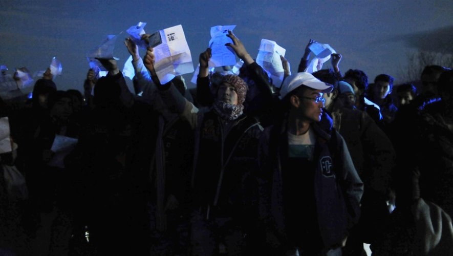 Des réfugiés afghans tendent leurs papiers d'identité près du village d'Idomeni, alors que la police grecque refuse de les laisser passer la frontière de Macédoine, le 21 février 2016