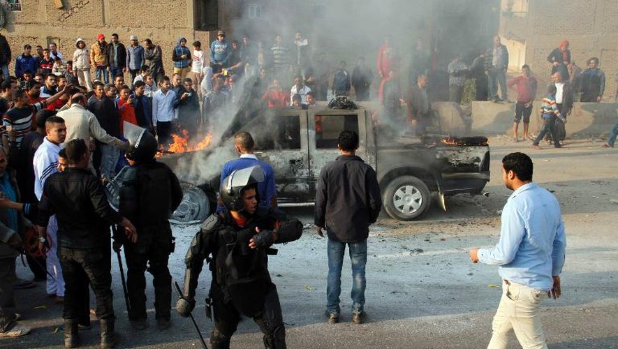 Des Egyptiens observent une voiture de police incendiée par des partisans du président déchu Mohamed Morsi en marge d'une manifestation, le 3 janvier 2014 au Caire
