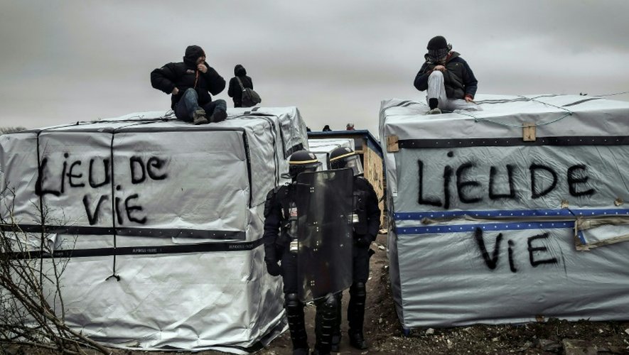 Des policiers se tiennent près de migrants sur les toits d'abris dans la "jungle" de Calais, le 1er mars 2016