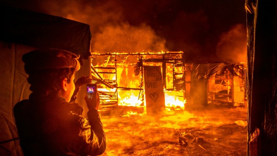 Un jeune migrant afghan filme avec son téléphone portable un incendie dans un abri de fortune de la "jungle" de Calais, devant lequel une pancarte indique "lieu de vie", le 1er mars 2016
