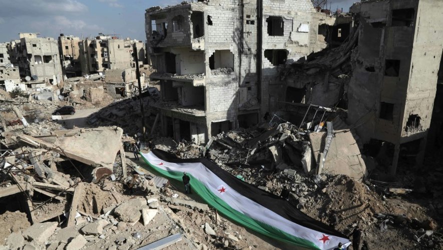 Des habitants et et des militants déploient un drapeau géant de la rébellion syrienne, lors d'une manifestation dans les décombres du quartier de Jobar, dans l'est de Damas, le 3 mars 2016