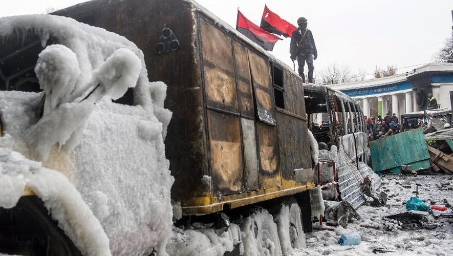 Un opposant ukrainien est juché sur un autobus incendié qui sert de barricade devant les forces de l'ordre, le 21 janvier 2014 à Kiev