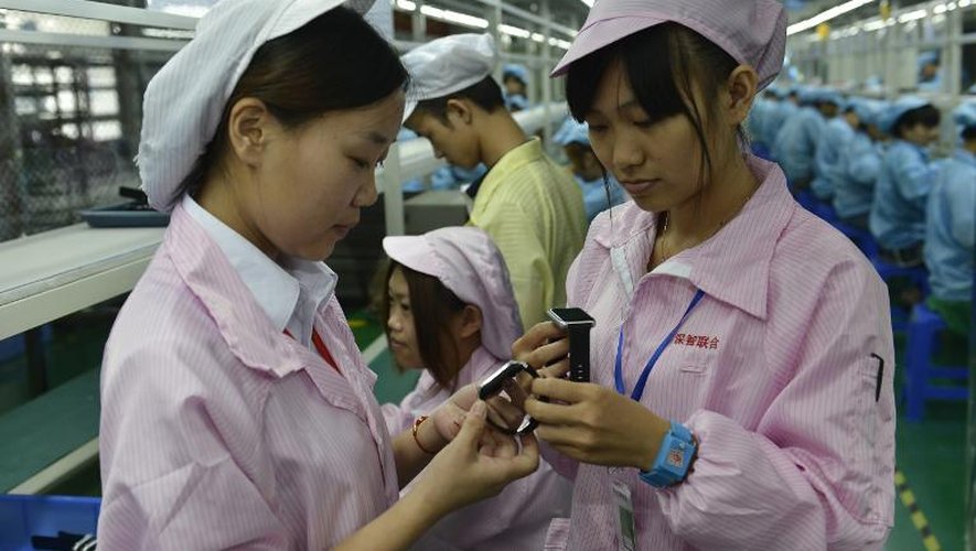 Deux ouvrières observent des montres  concurrentes de l'Apple Watch fraîchement sorties de la chaîne de fabrication, le 22 avril 2015 dans une usine de Shenzhen, dans le sud de la Chine