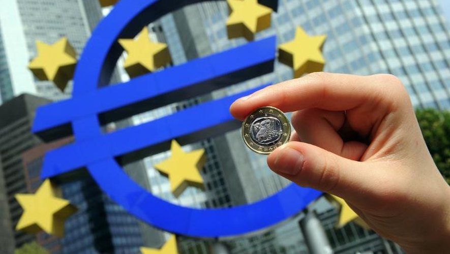 Une femme tient une pièce d'un euro devant le symbole de la monnaie unique placé à côté de l'ancien siège de la BCE à Francfort, le 29 avril 2010