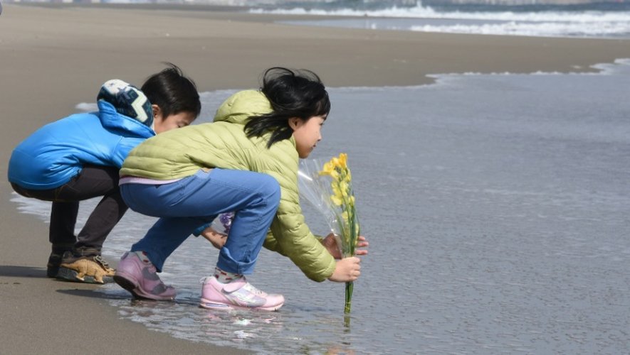 Des enfants déposent des fleurs sur la plage de Sendai, au Japon, le 11 mars 2016, en hommage au victimes du séisme et du tsunami de 2011