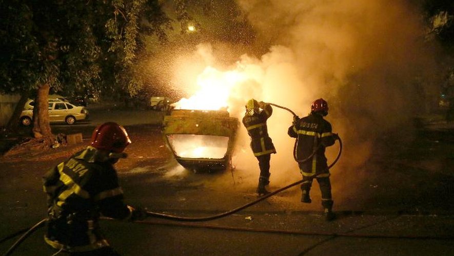 Des pompiers éteignent un véhicule en feu lors d'affrontements entre manifestants et police dans le quartier du Chaudron, le 30 janvier 2014 à Saint-Denis de La Réunion