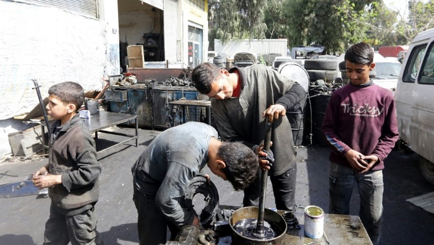 Othman al-Najjar (2e d) et son frère Rasheed (c) travaillent dans un garage à Damas, le 10 mars 2016