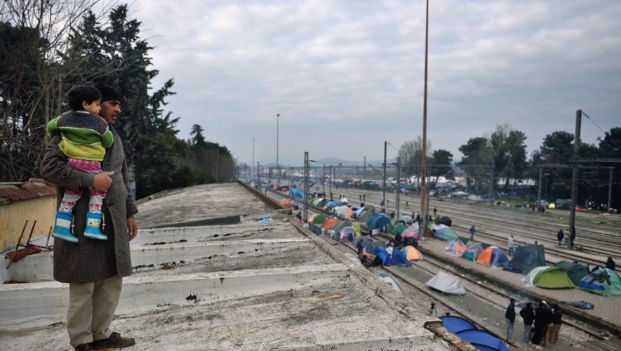 Un migrant et sa fille regardent les tentes abritant des réfugiés installées sur les quais et voies ferrées de la gare d'Idomeni, à la frontière gréco-macédonienne, le 17 mars 2016