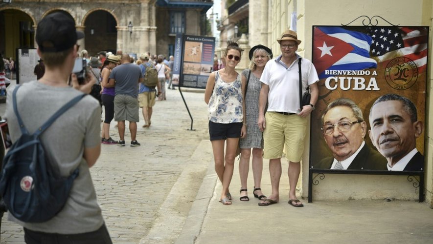 Des touristes posent devant une photo de Obama et Castro, le 19 mars 2016, à l'entrée d'un restaurant à la Havane, la veille de l'arrivée historique du président américain à Cuba