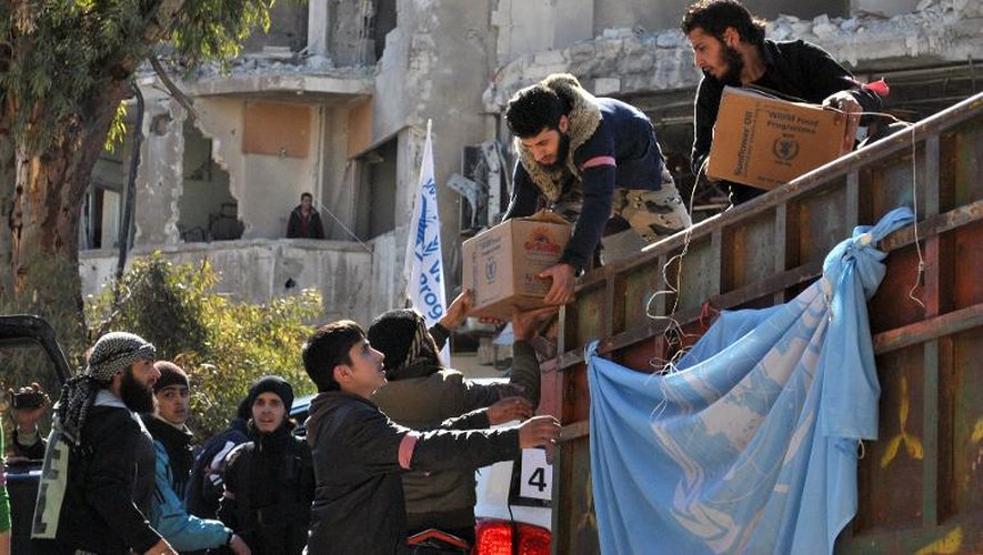 Des rebelles syriens déchargent des cartons d'aide alimentaires lors d'une opération humanitaire dans les quartiers assiégés de Homs, le 12 février 2014