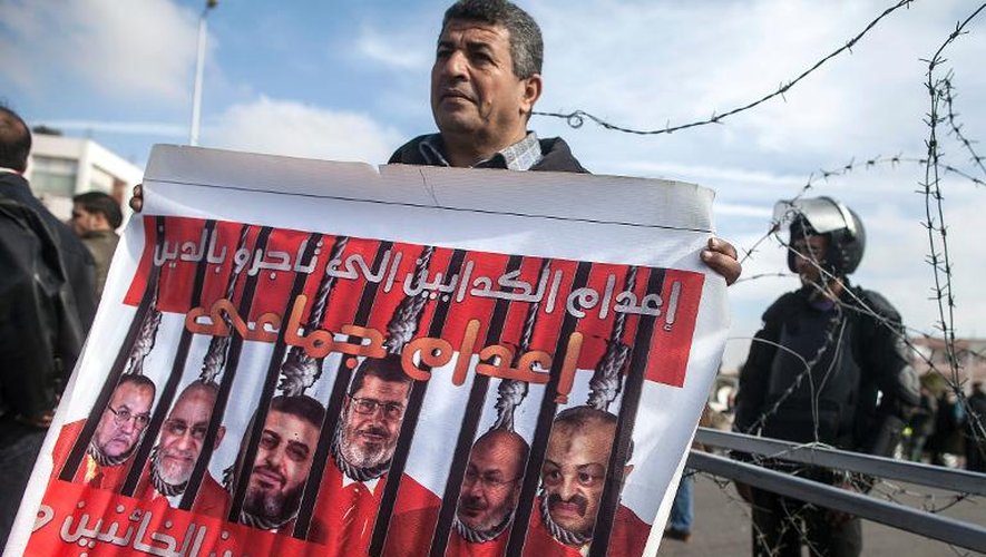 Un manifestant brandit une banderole montrant le président destitué Mohamed Morsi avec ses co-accusés, devant le siège de la police du Caire, le 1er février 2014