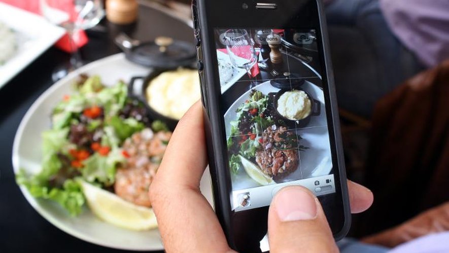 Un homme prend en photo son plat avec son smartphone dans un restaurant à Paris