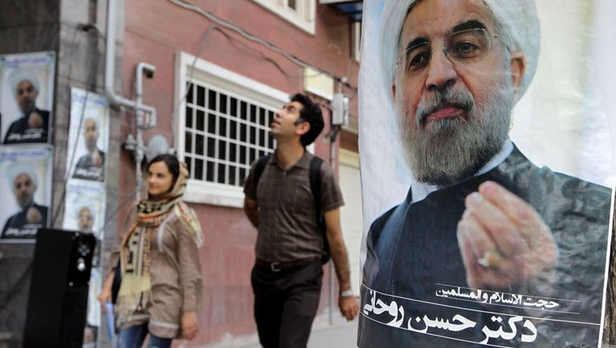Des Iraniens marchent à côté de l'affiche de campagne du candidat Hassan Rowhani, le 1er juin 2013 à Téhéran