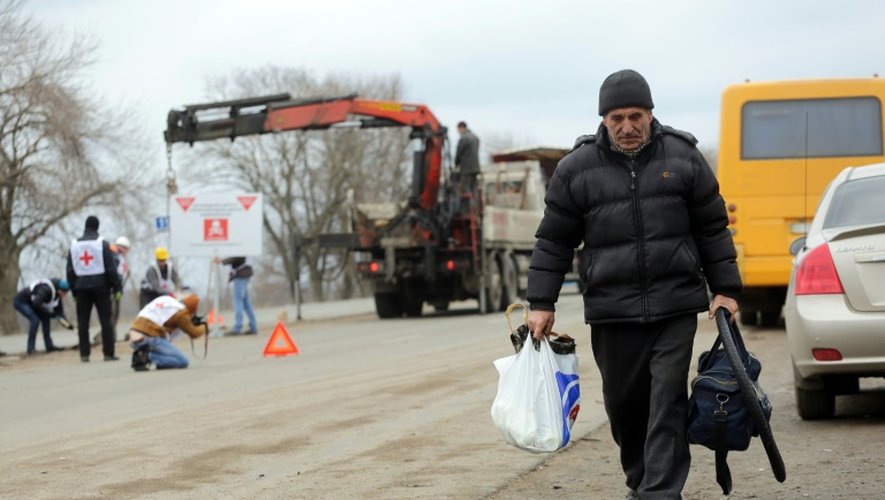 Un habitant du village de Berezové, dans la région de Donetsk, marche sur le bord d'une route, le 28 mars 2016, alors que des agents de la Croix-rouge installent des panneaux de prévention contre les mines "Danger de mines! Ne quittez pas la route!"