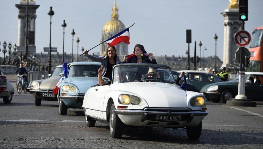 Les occupants d'une DS agitent le drapeau français près du pont Alexandre III le 24 mai 2015 à Paris pour célébrer le 60e anniversaire de la voiture mythique de Citroën