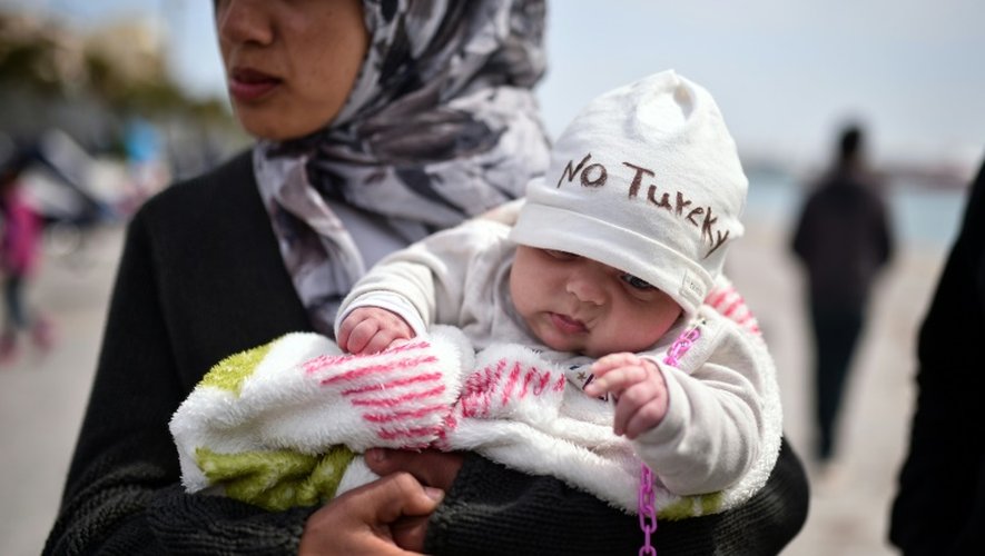 Dans les bras de sa mère migrante, un bébé porte un bonnet où il est écrit "No Turkey"