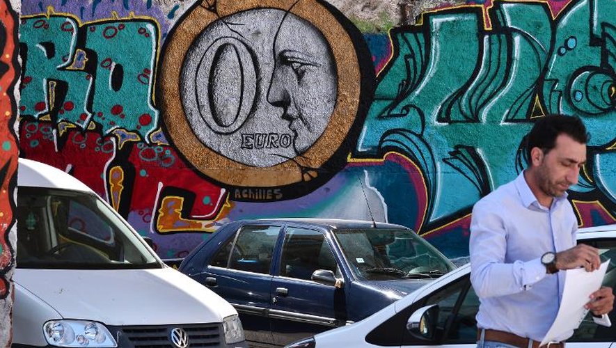 Un homme marche le 25 mai 2015 devant un graffiti montrant une pièce de "0 euro" dessiné sur le mur d'un parking d'Athènes