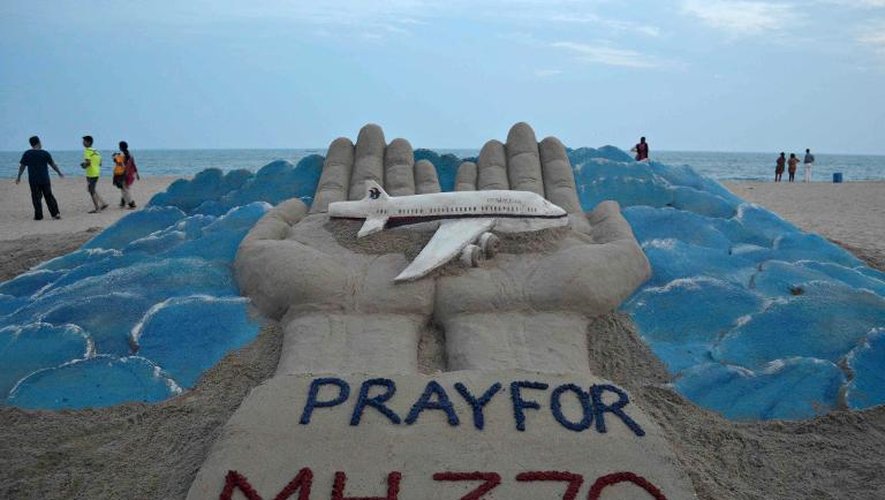 Des promeneurs passent sur une plage à Puri en Inde où l'artiste Sudersan Pattnaik a sculpté dans le sable un mémorial aux victimes du vol MH370, le 12 mars 2014