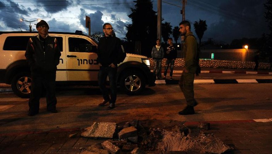 Des soldats et des civils israéliens près d'un trou causé par une roquette lancée depuis la bande de Gaza, à Sderot le 12 mars 2014