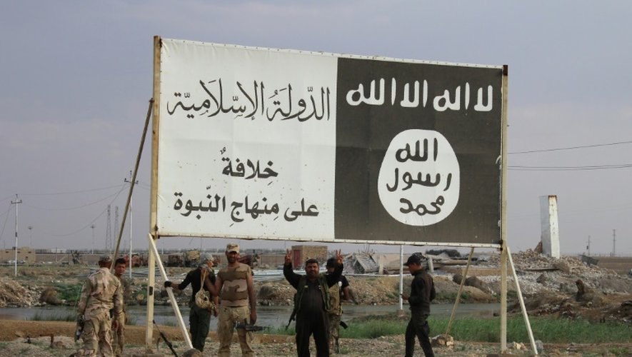 Des soldats irakiens se regroupent près d'un panneau publicitaire couvert de slogans et du drapeau de l'Etat islamique, à Hit, le 7 avril 2016, alors qu'ils viennent de reprendrent la ville aux mains des jihadistes