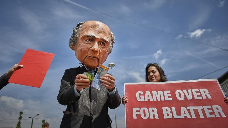 Un homme porte un masque au visage du président de la Fifa, Sepp Blatter, qui tient des francs suisses dans les mains tandis qu'une manifestante brandit une pancarte "le jeu est terminé pour Blatter" devant le Hallenstadium où se tient le 65è Congrès de la Fifa