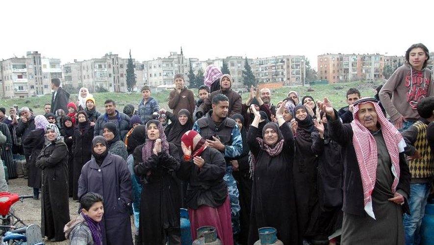Des femmes, des hommes et des enfants attendent l'aide du gouvernement près de Homs le 13 mars 2014