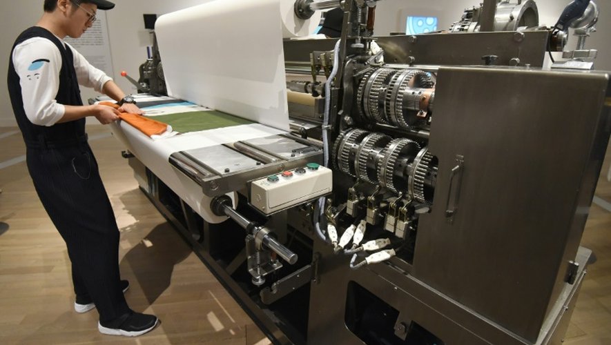 Un employé du  styliste japonais Issey Miyake travaille sur une machine à faire des plis le 15 mars 2016 au National Art Center à Tokyo
