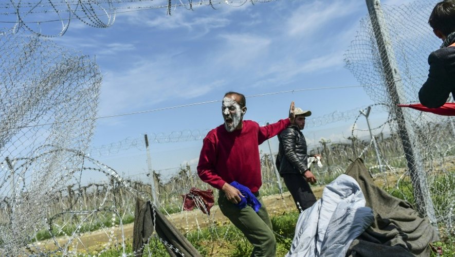 Un homme enjoint les réfugiés et les migrants à traverser la grille de fer à la frontière gréco-macédonienne dans le village grec d'Idomeni le 10 avril 2016