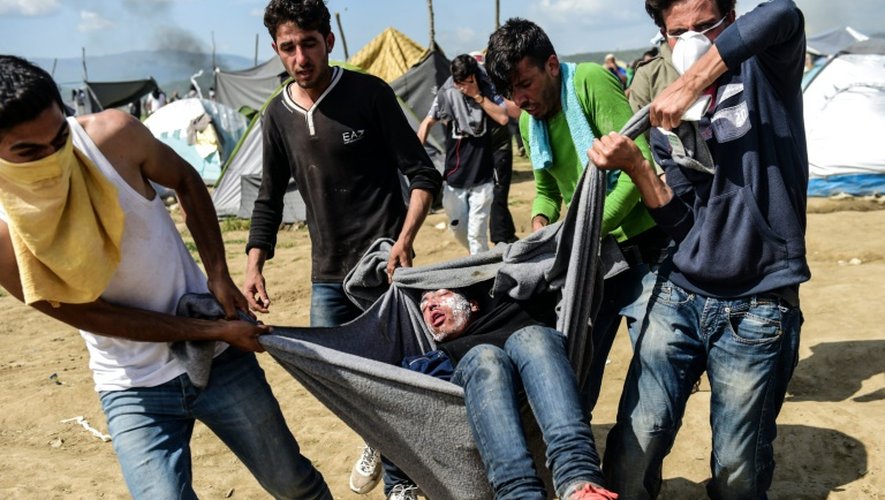 Des migrants transportent un homme blessé lors de heurts avec la police, en tentant en vain de franchir la frontière gréco-macédonienne à Idomeni, le 10 avril 2016