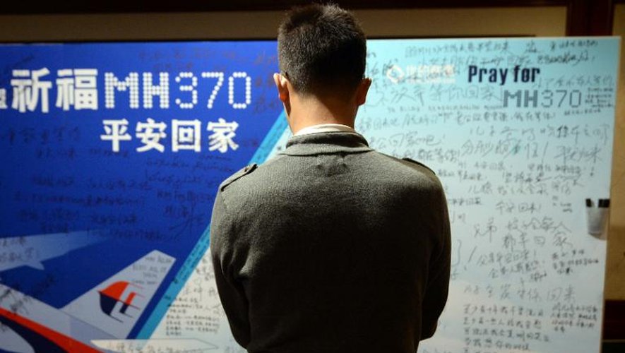 Un homme lit les messages écrits sur un panneau par les proches des passagers disparus du vol MH370, à Pékin le 22 mars 2014