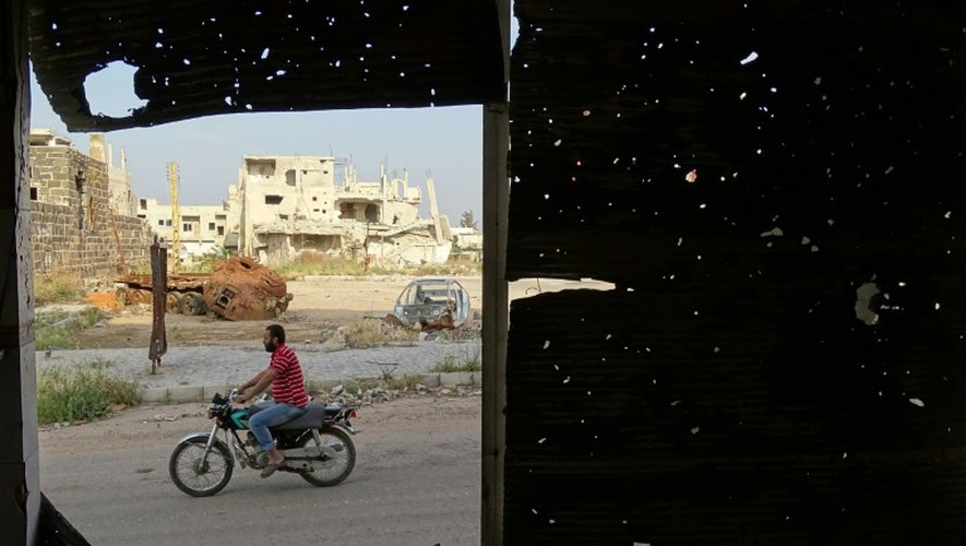 Un homme sur une mobylette vu à travers un volet d'une fenêtre criblée de balles dans une zone tenue par des rebelles à Daraa dans le sud de la Syrie le 15 avril 2016