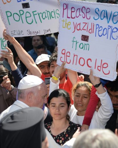 Des femmes brandissent des pancartes appellant à sauver du génocide le peuple Yazidi, lors de la visite du pape François sur l'île de Lesbos, le 16 avril 2016