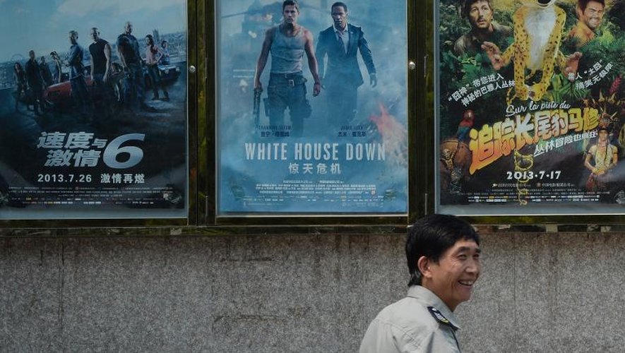 Un homme passe devant des affiches de films, dont celle de la comédie française "Sur la piste du marsupilami" (à droite), sur la façade d'un cinéma à Pékin, en juillet 2013