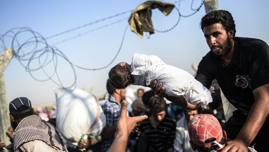 Un Syrien fait passer un enfant par-dessus les grillages séparant la Syrie de la Turquie, pour fuir les combats en Syrie, le 14 juin 2015, au poste-frontière de Akcakale
