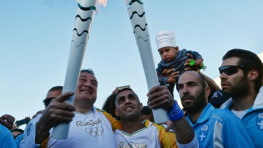 Le président du comité héllenique olympique, Spyros Kapralos (gauche) remet la flamme olympique au réfugié syrien Ibrahim al-Hussein (centre), un nageur amputé, le 26 avril 2016 à Athènes