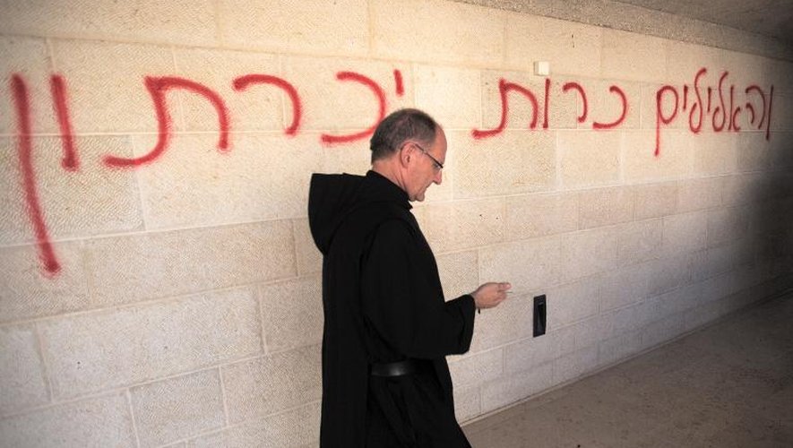 Un prêtre passe devant un mur du sanctuaire de Tabgha, sur les rives du lac de Tibériade, portant un graffiti en hébreu biblique qui appelle à chasser d'Israël les dieux païens
