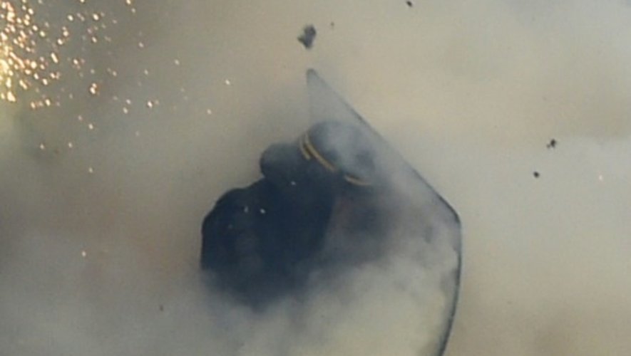 Un policier anti-émeute se protège de fumigènes jetés par des manifestants à Paris, le 28 avril 2016