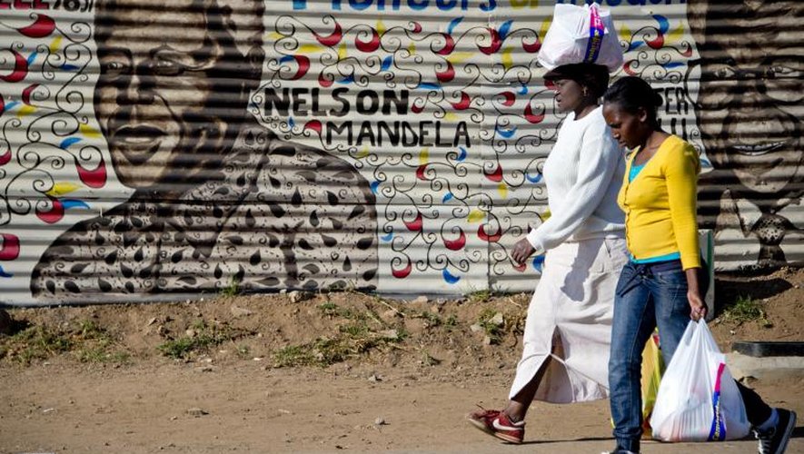 Deux femmes passent devant un portrait de Nelson Mandela sur un mur de Soweto en Afrique du Sud, le 30 juin 2013