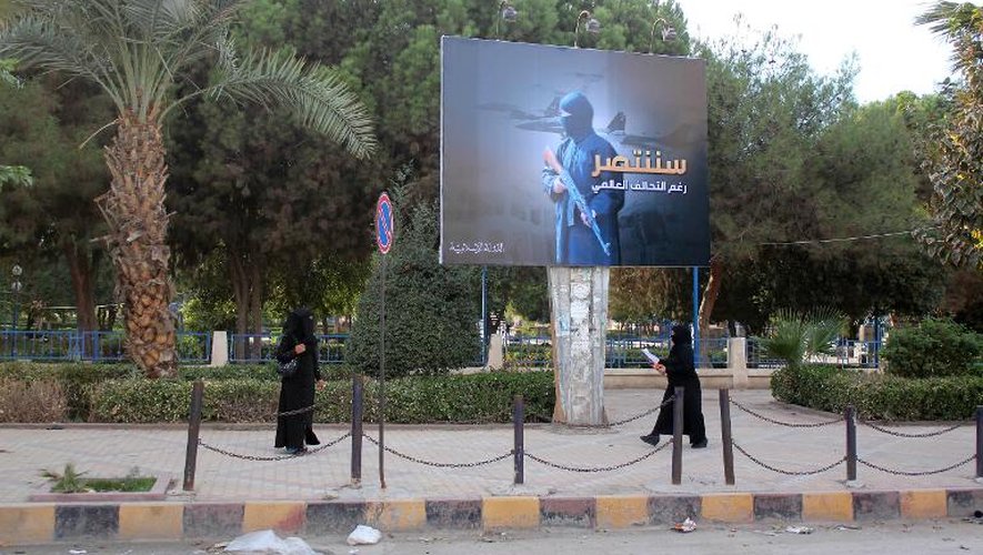 Des femmes entièrement voilées marchent devant un panneau du groupe jihadiste EI proclamant "Nous serons victorieux", le 1er novembre 2014 dans la ville de Raqa, en Syrie