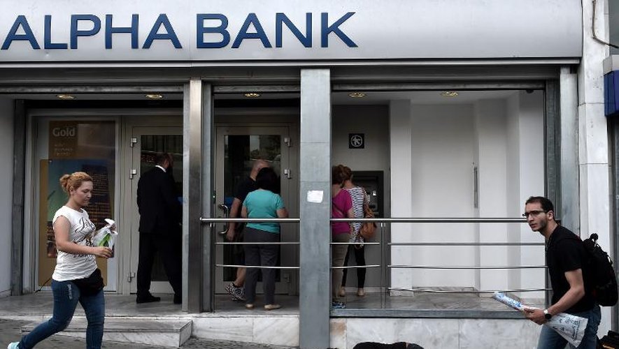 Des épargnants tirent de l'argent alors qu'un SDF dort par terre devant une banque, le 19 juin 2015 dans le centre d'Athènes