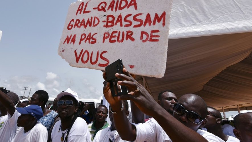 Des Ivoriens portent une pancarte "Al-Qaïda, Grand-Bassam n'a pas peur de toi", lors d'un hommage aux victimes de l'attaque jihadistes du 13 mars 2016 qui a fait 19 morts, le 20 mars 2016 à Grand-Bassam en Côte d'Ivoire