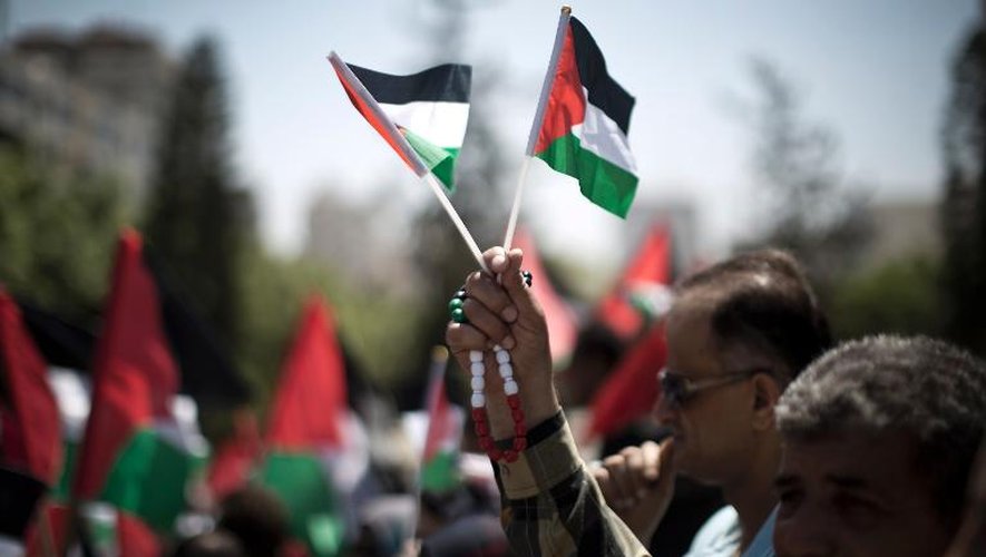 Un Palestinien brandit des drapeaux nationaux lors d'une manifestation en faveur d'une autre tentative de réconciliation entre les rivaux, le mouvement islamiste Hamas et l'organisation de libération de la Palestine (OLP) le 22 avril 2014 à Gaza
