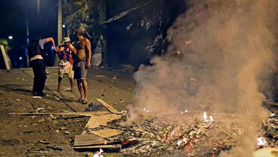 Après la fin des affrontements dans une favela près de Copacabana à Rio de Janeiro le 22 avril 2014, des odeurs s'échappent de tas d'ordures enflammés, un policier contrôle un habitant